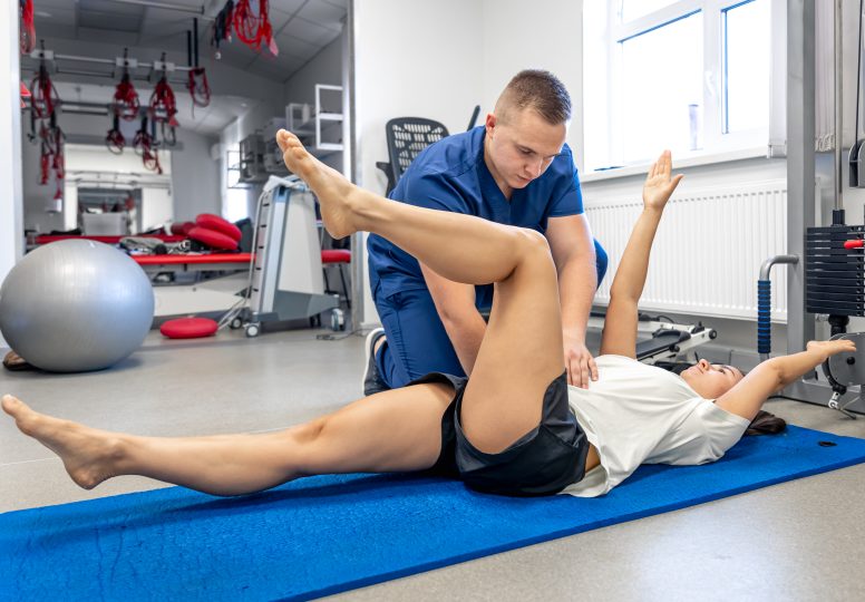 Woman doing gymnastics with help of his young physical therapist.
